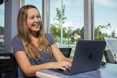 A UWF student smiles while using a laptop indoors.